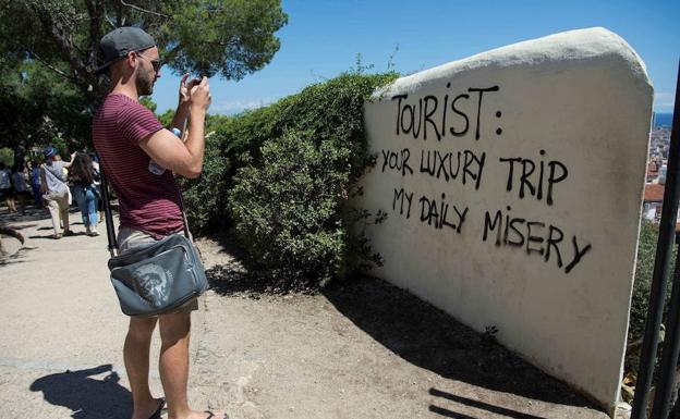 Un turista junto a una pintada en una pared que dice 'Turista: tu viaje de lujo mi miseria diaria'. /Afp