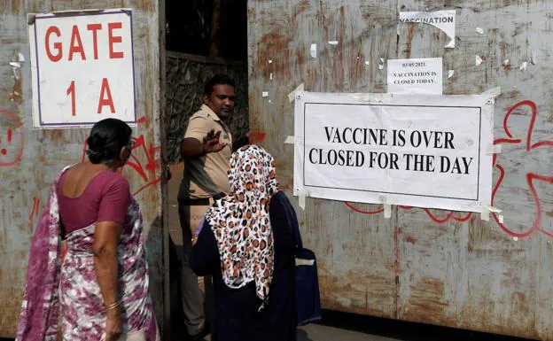 Un policía impide la entrada a dos mujeres en un centro de vacunación de Bombay tras agotarse las dosis. /REUTERS